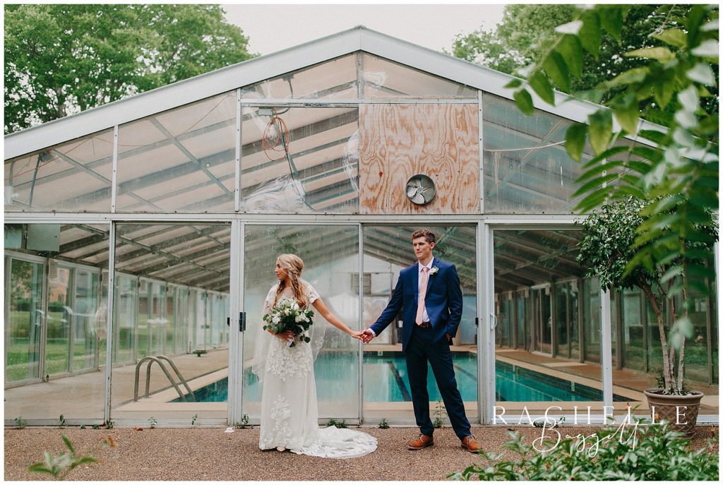 bride and groom stand in front of greenhouse