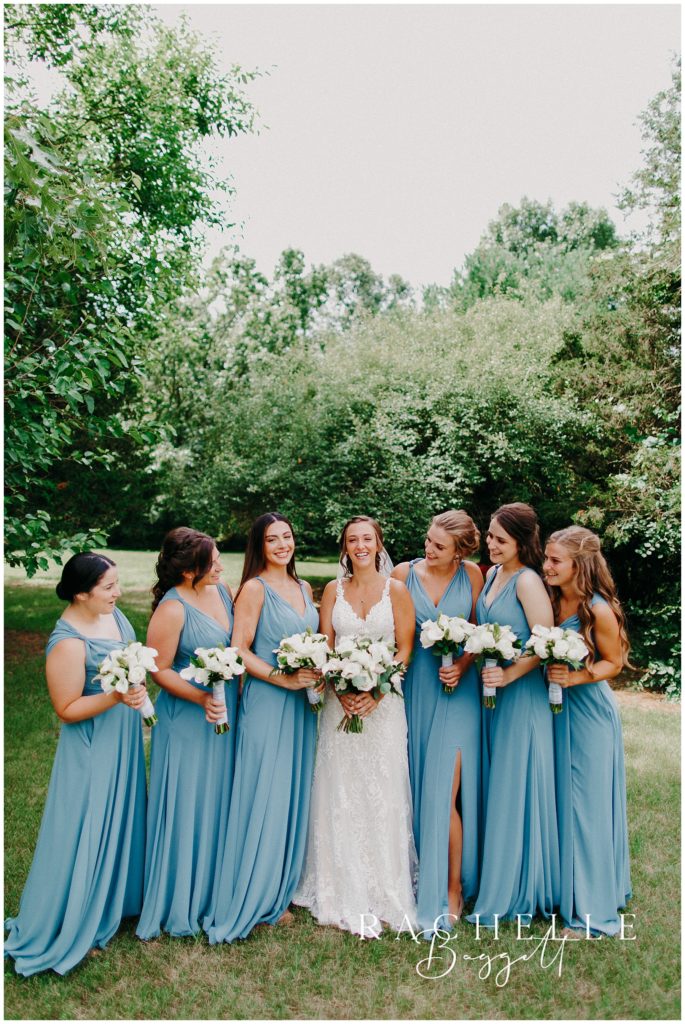a bride and bridesmaids stand and smile in a field