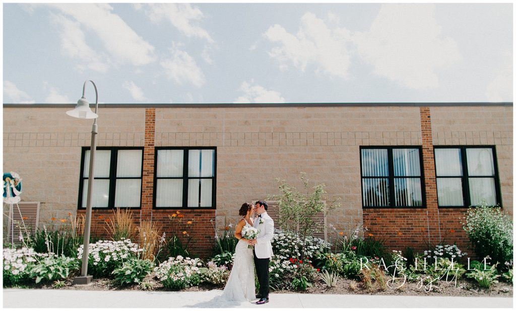 bride and groom stand in front of building and kiss