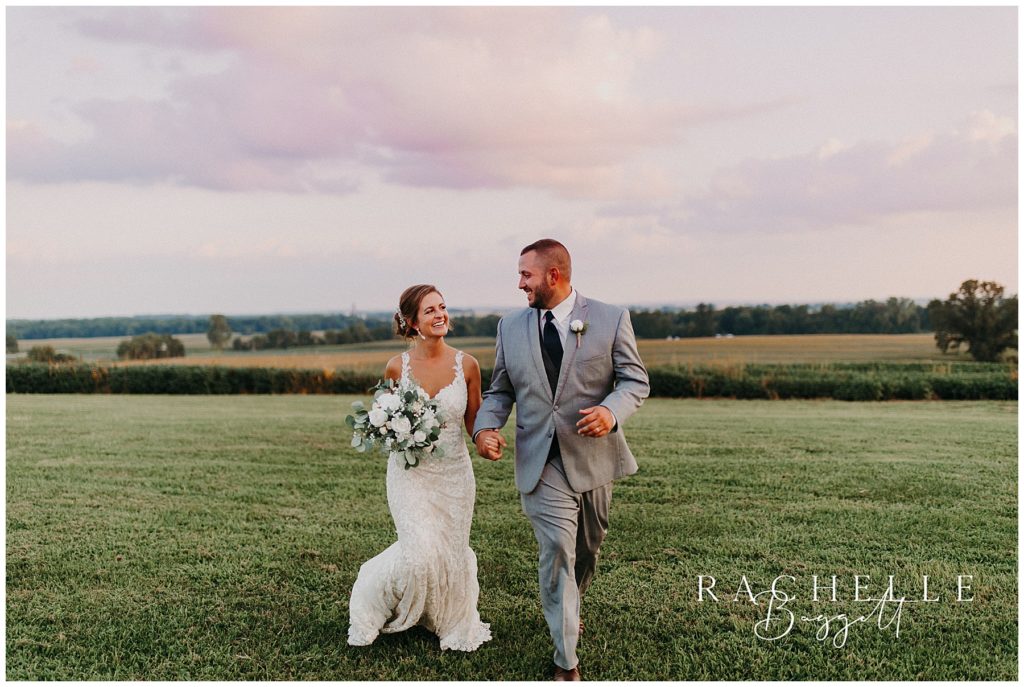 Bride and groom run through field and smile.