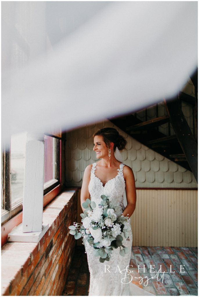 a bride looks out the window while holding flowers. Evansville Wedding Photographer.