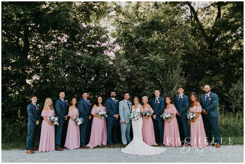 a bridal party stands in front of trees and smiles. Evansville Wedding Photographer.