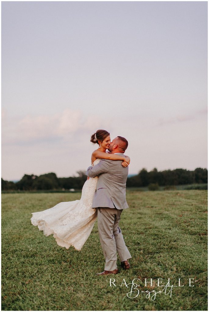a man and woman kiss in a field while he twirls her. 