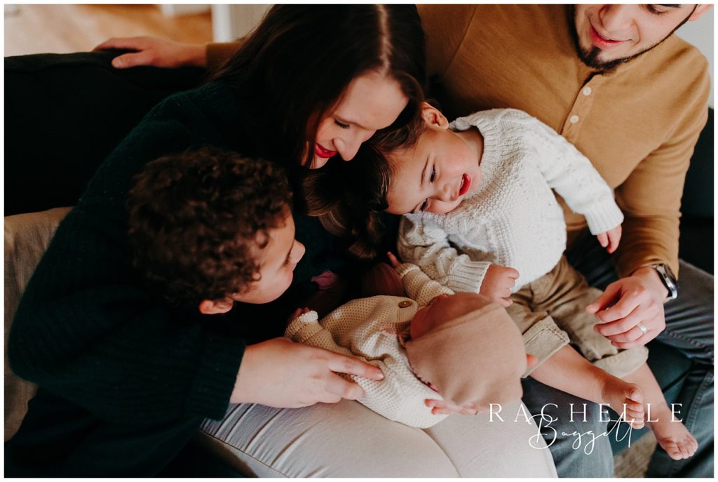mom, dad and brothers look adoringly at their new sister in cozy session