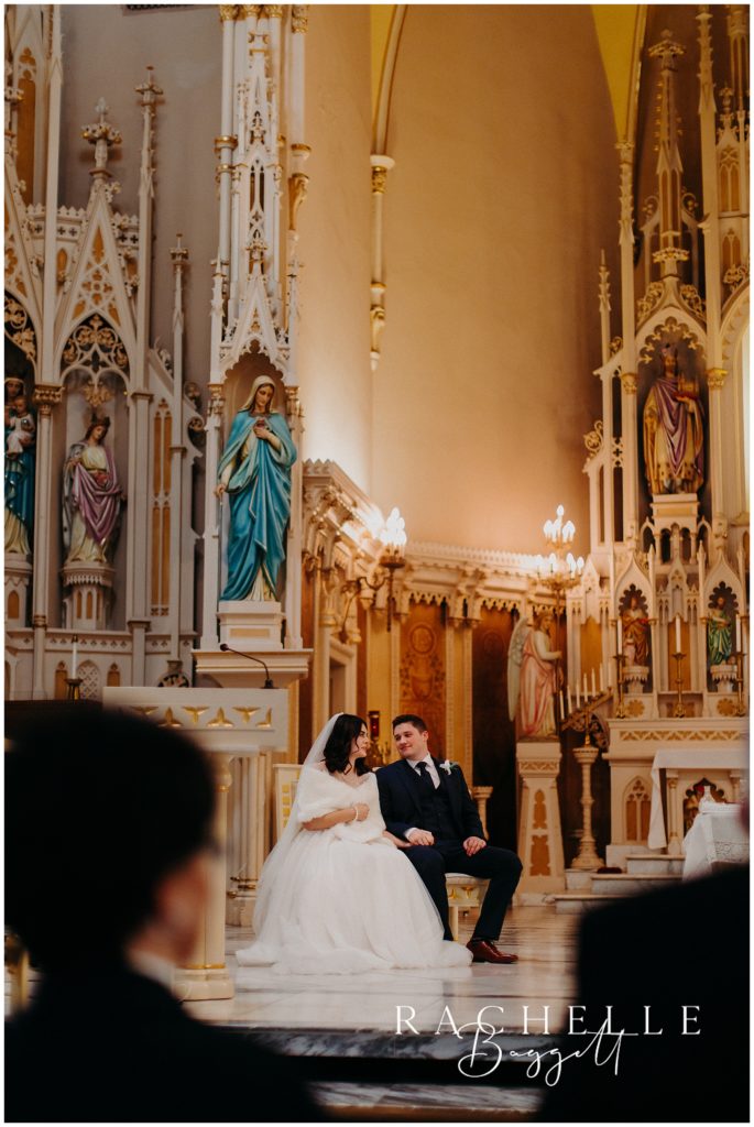 new husband and wife sitting next together surrounded by beautiful cathedral decor