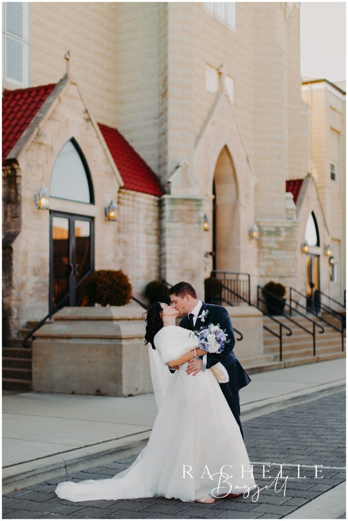 husband and wife share an elegant kiss outside the front of the parish