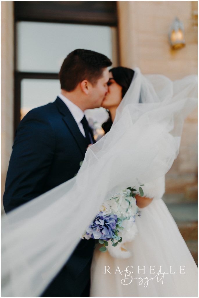 husband and wife kiss, veil blowing in the wind