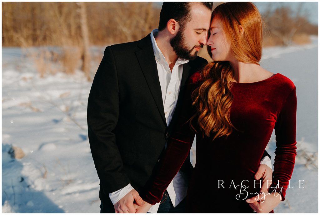 man and woman touch noses during their snowy sunrise engagement session