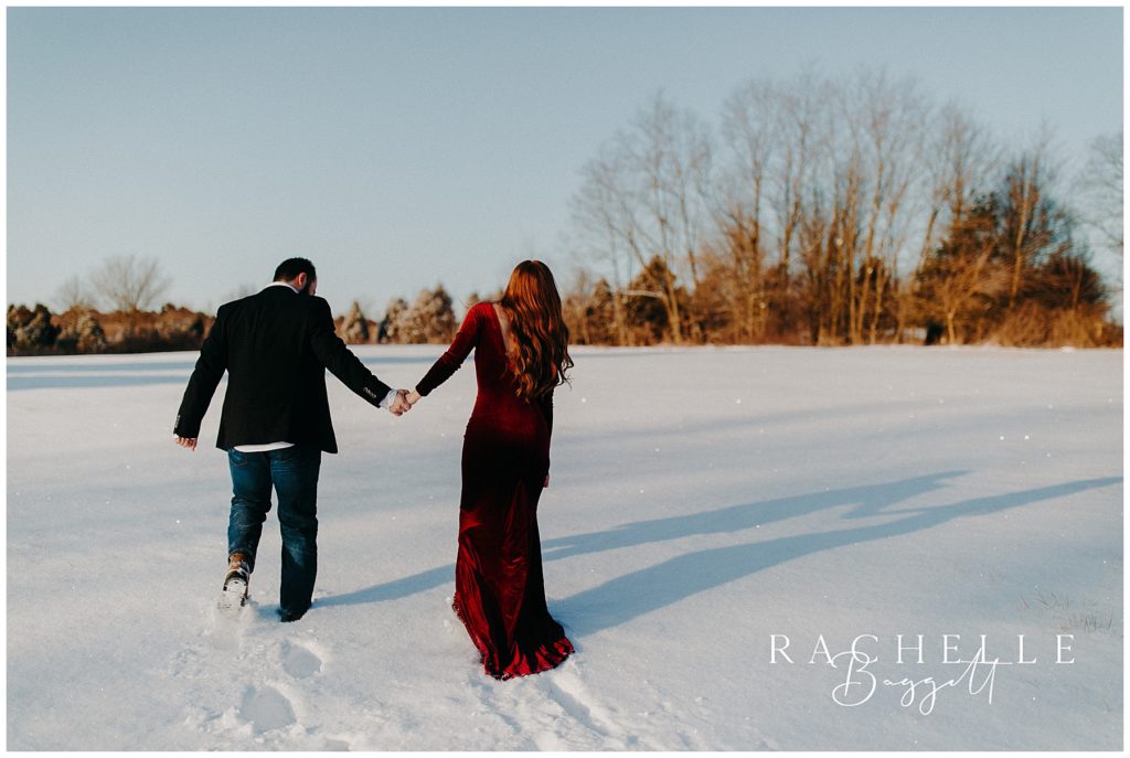 man and woman in elegant red dress walk across the snow together