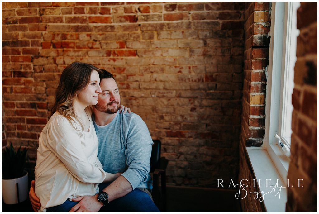 husband and wife gaze out window during Downtown Loft Couples Session