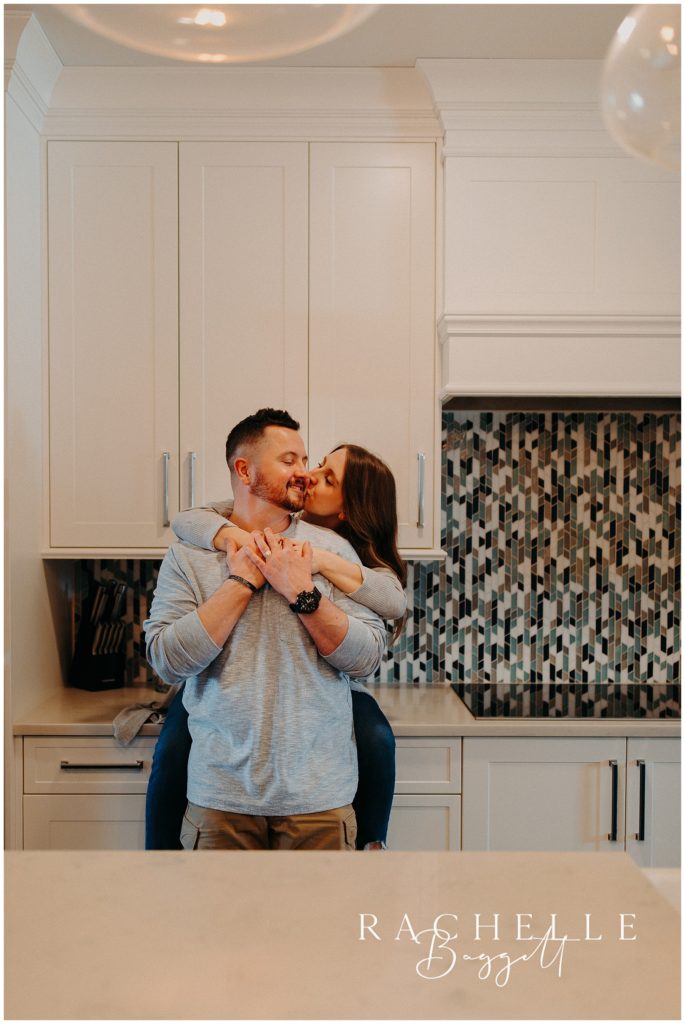 kitchen backdrop of downtown loft with wife kissing husband on cheek