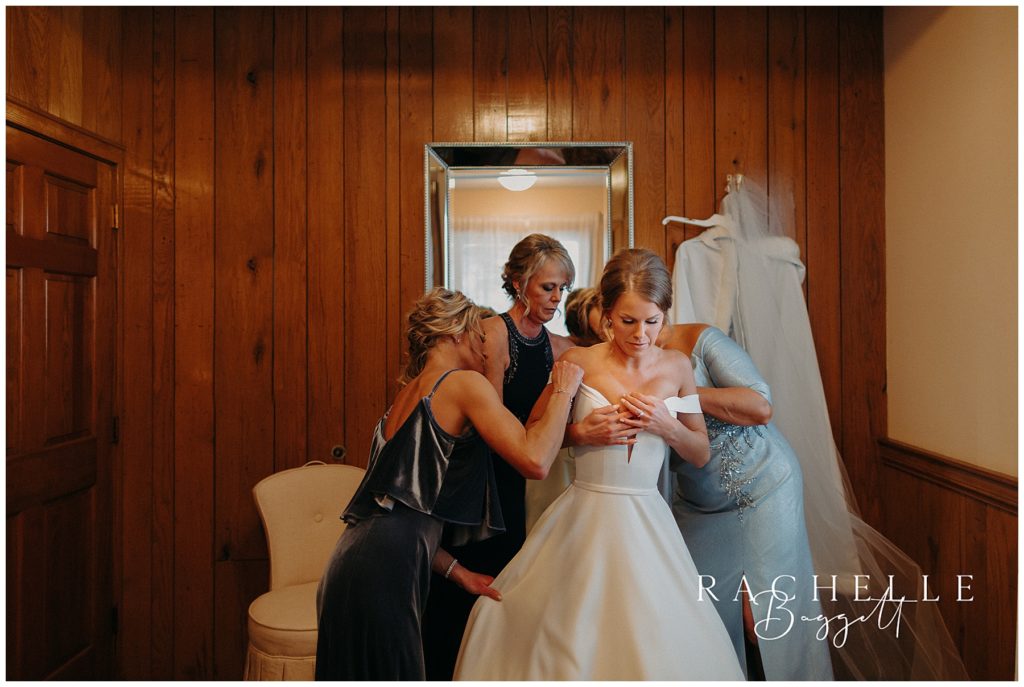family helping bride get into wedding dress