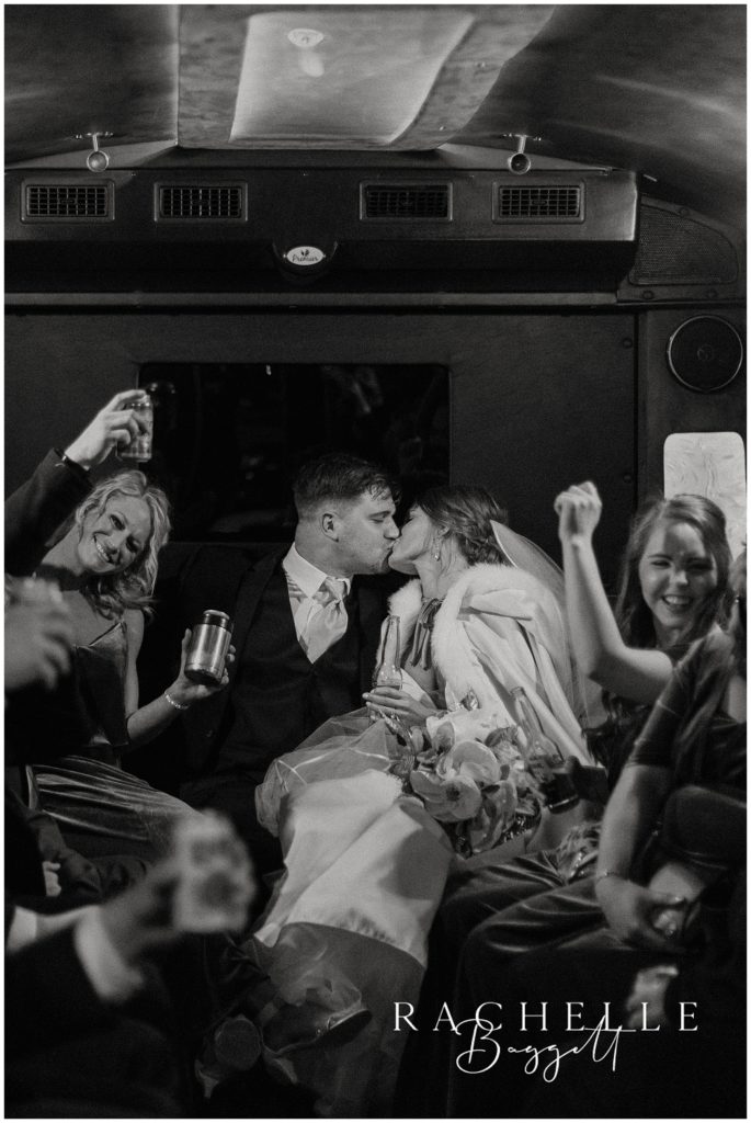 husband and wife share a kiss in the limo while wedding party cheers