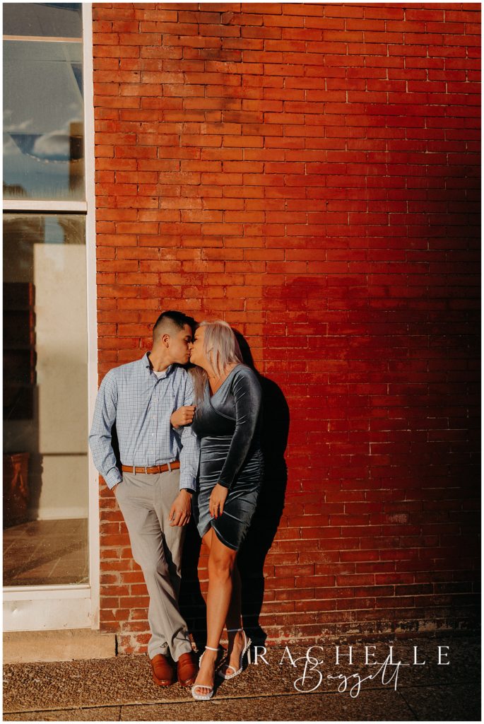 man and woman kiss in front of brick wall