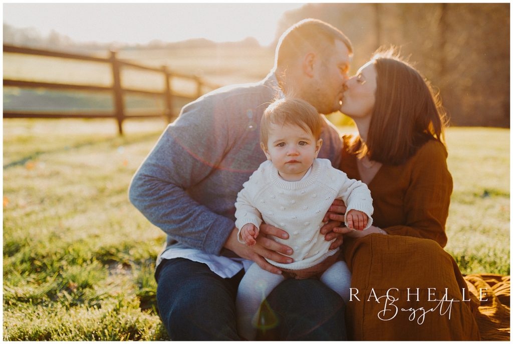 mom and dad kiss while holding baby during Sunrise Family Session