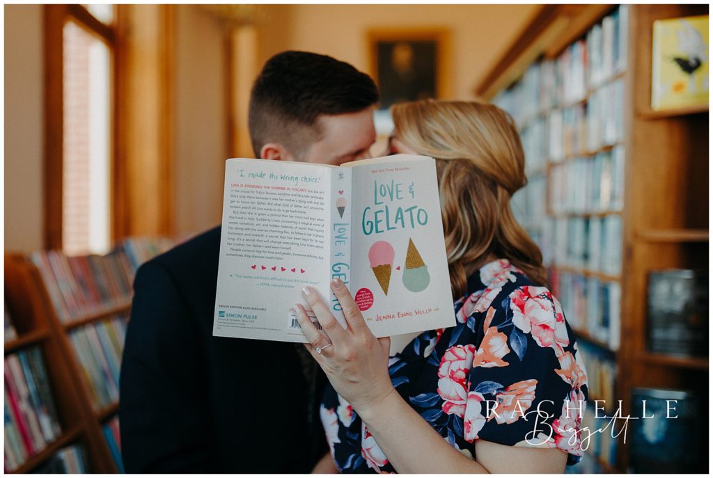 couple kisses behind book during Intimate Willard Library Engagement