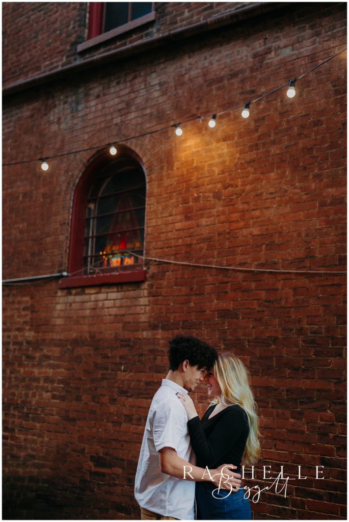 man and woman nuzzle each other outside a rich, textured brick wall downtown