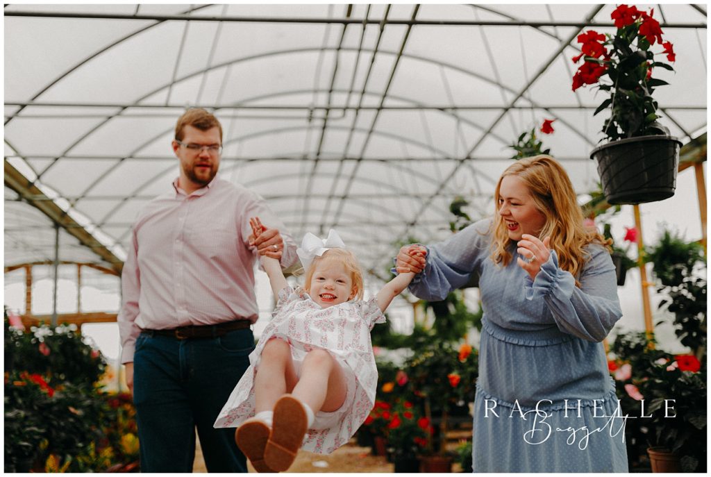 mom and dad swinging daughter playfully during Sweet Greenhouse Family Mini