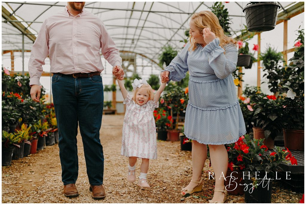 parents swinging daughter  playfully in greenhouse aisle