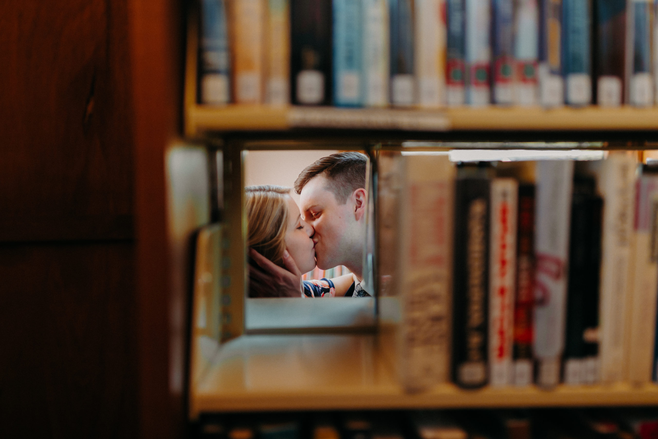 Man and woman kiss next to bookshelf